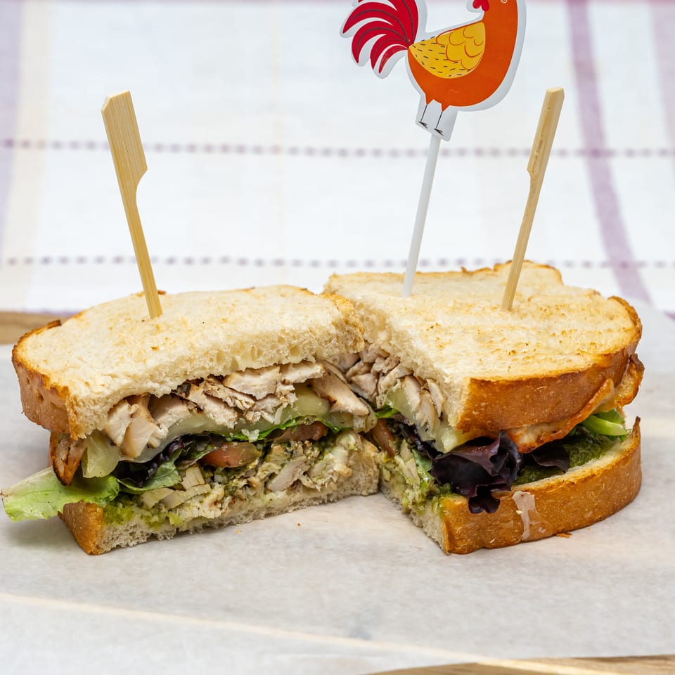 Cut chicken salad sandwich on toasted bread, layered with lettuce, tomato, cucumber, and creamy dressing, secured with picks.
