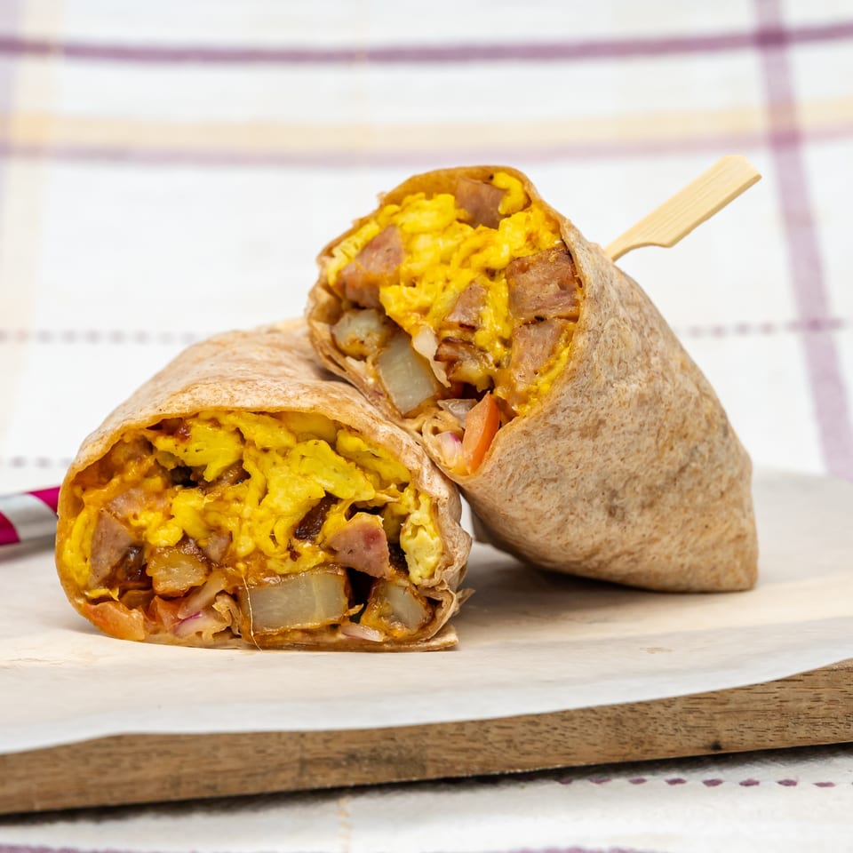Two grilled breakfast burritos filled with scrambled eggs, sausage, potatoes, and melted cheese on a wooden serving board.