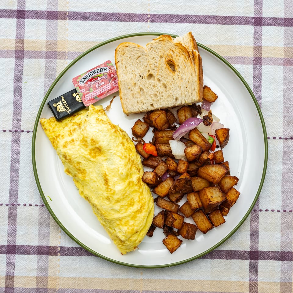 Breakfast plate with a folded omelet, roasted potatoes with peppers and onions, toast, butter, and strawberry jam.